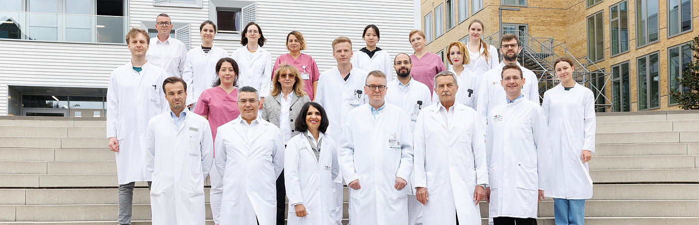 Teamfoto des Interdisziplinären Gefäßzentrums der UMM mit den Mitarbeitenden in zwei Reihen vor einem Klinikgebäude.