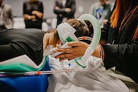 Person in Bauchlage mit Schlauch und Maske am Kopf. 