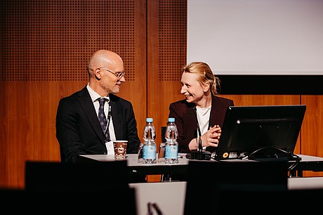 Zwei Personen diskutieren während einer Sitzung auf der Bühne.