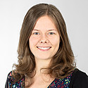 Eine junge Frau vor hellem Hintergrund blickt lächelnd in die Kamera