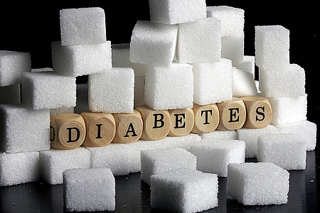 Das Foto ist ein Symbolbild für die Krankheit Diabetes, es zeigt den Begriff ausgeschrieben auf Holzwürfelchen in einem Berg von Zuckerwürfeln