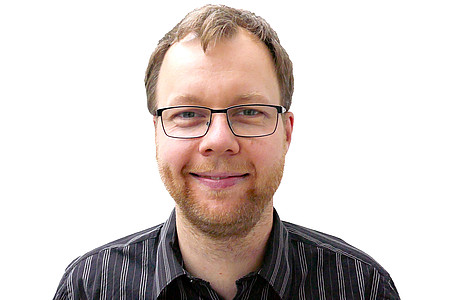 Das Bild zeigt ein Portraitfoto von Herrn Dr. Solinski, eines jungen Mannes mit Brille und dunklem Hemd