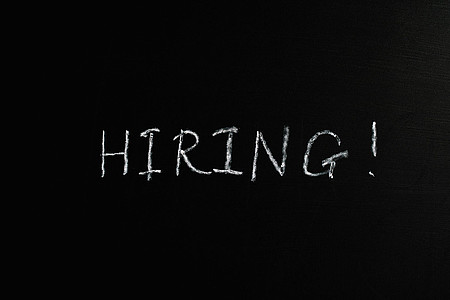 Das Wort 'HIRING!' in weißer Kreideschrift auf schwarzem Hintergrund