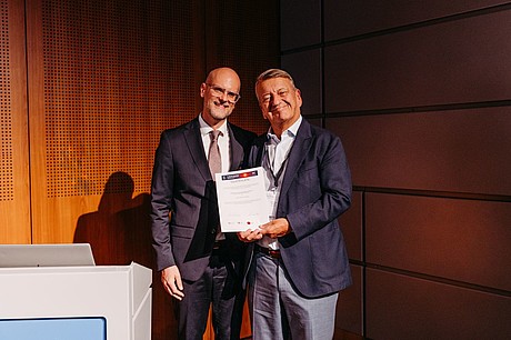 Zwei Männer bei der Übergabe einer Urkunde auf der Bühne des ZKAM-Meetings.