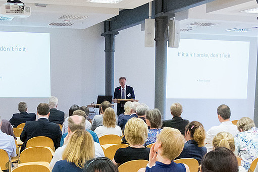 Hörsaal mit sprechender Person am Rednerpult