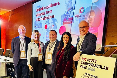 Fünf Personen mit Namensschildern stehen vor einer Bühne mit einem großen Bildschirm und einem Schild mit der Aufschrift 'ESC ACUTE CARDIOVASCULAR CARE 2026 20-21 MARCH LISBON, PORTUGAL'