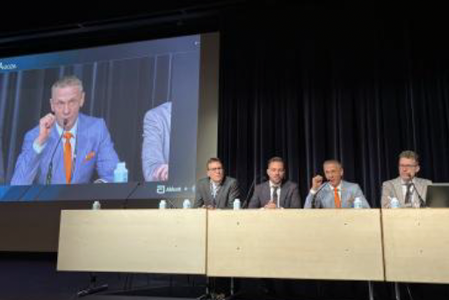 Podiumsdiskussion bei einem Fachkongress mit mehreren Personen auf der Bühne und einer Live-Übertragung auf einer großen Leinwand.