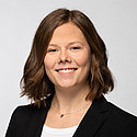 Eine junge Frau steht vor hellem Hintergrund und blickt lächelnd in die Kamera.
