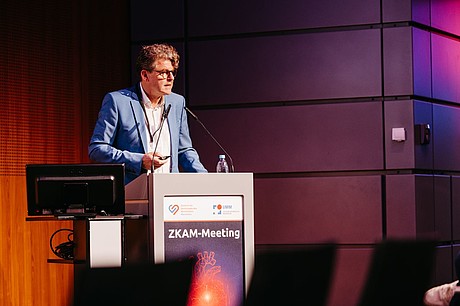 Ein Referent hält einen Vortrag am Rednerpult des ZKAM-Meetings.