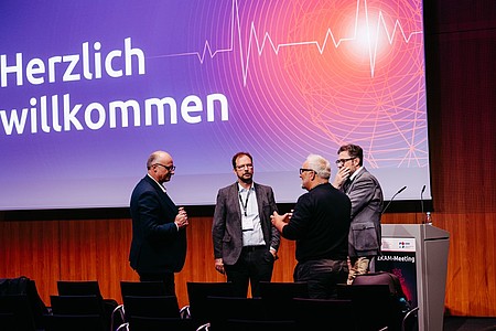 Mehrere Referenten bei der Begrüßung auf der Bühne des ZKAM-Meetings.