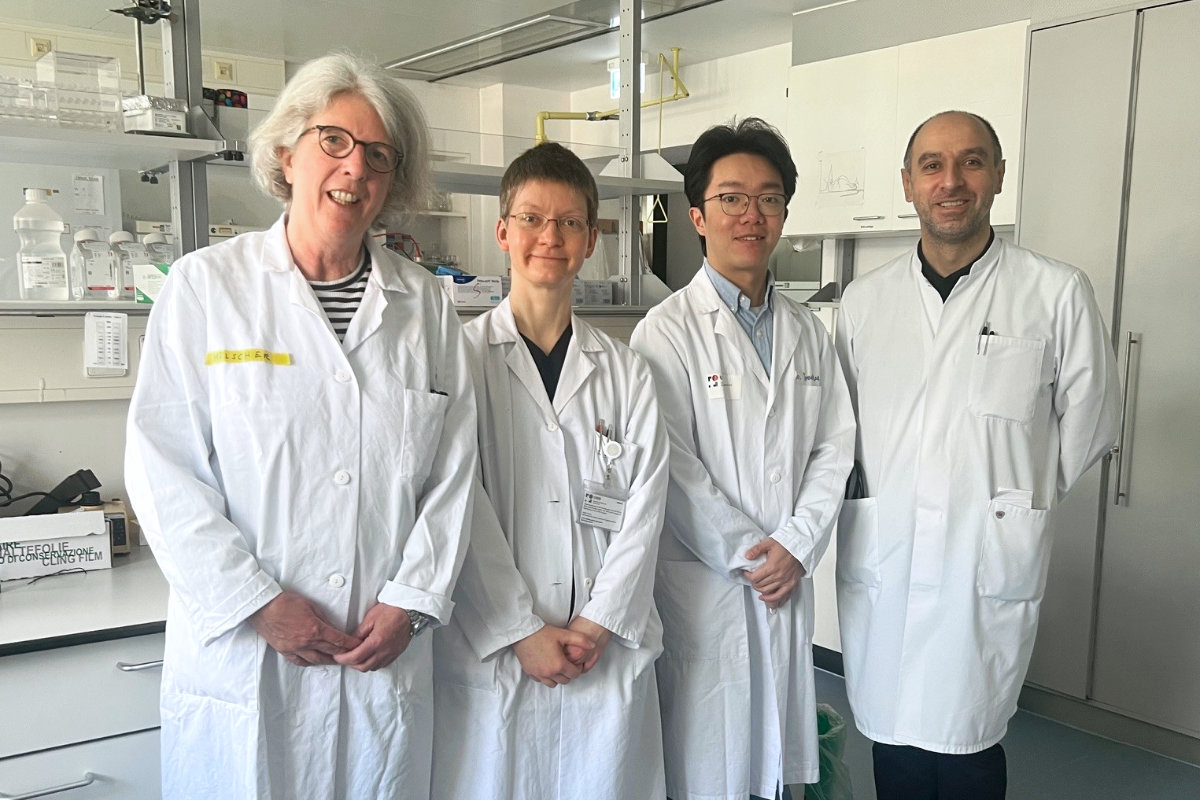 Vier Personen in weißen Laborkitteln stehen in einem Laborraum mit Schränken und Laborgeräten