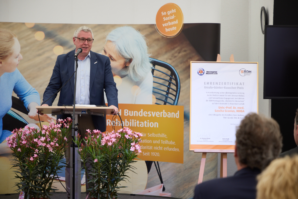 Mann im schwarzen Anzug hält Rede bei Preisverleihung