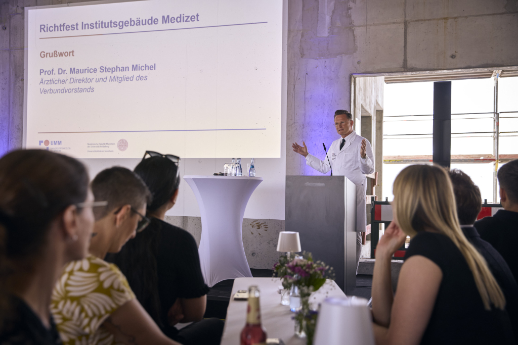 Professor Michel hält Ansprache: Mann im weißen Kittel steht auf Bühne und spricht zu Publikum