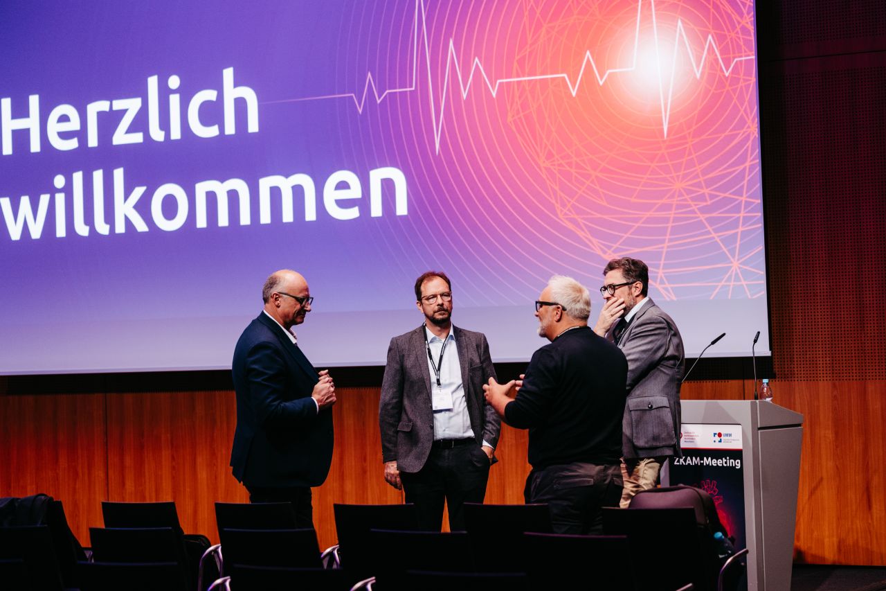 Mehrere Referenten bei der Begrüßung auf der Bühne des ZKAM-Meetings.